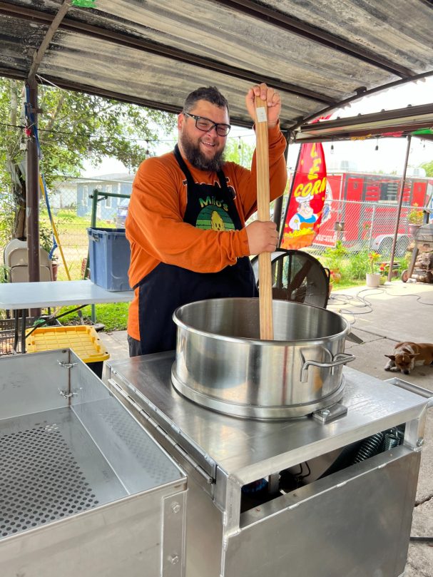 How We Started A person stirring a large pot on a stove in an outdoor cooking area.